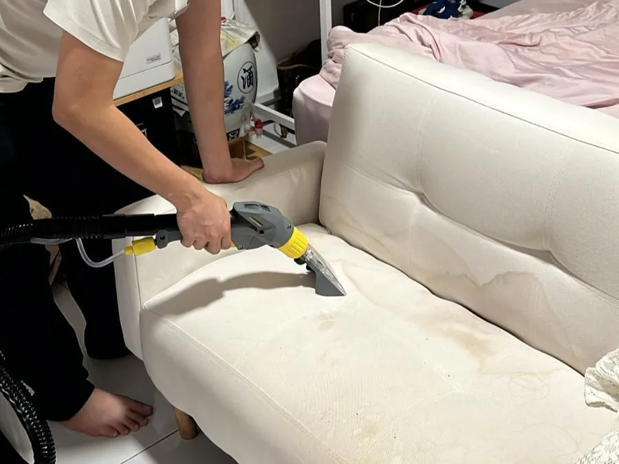 Technician steam cleaning a cream fabric sofa